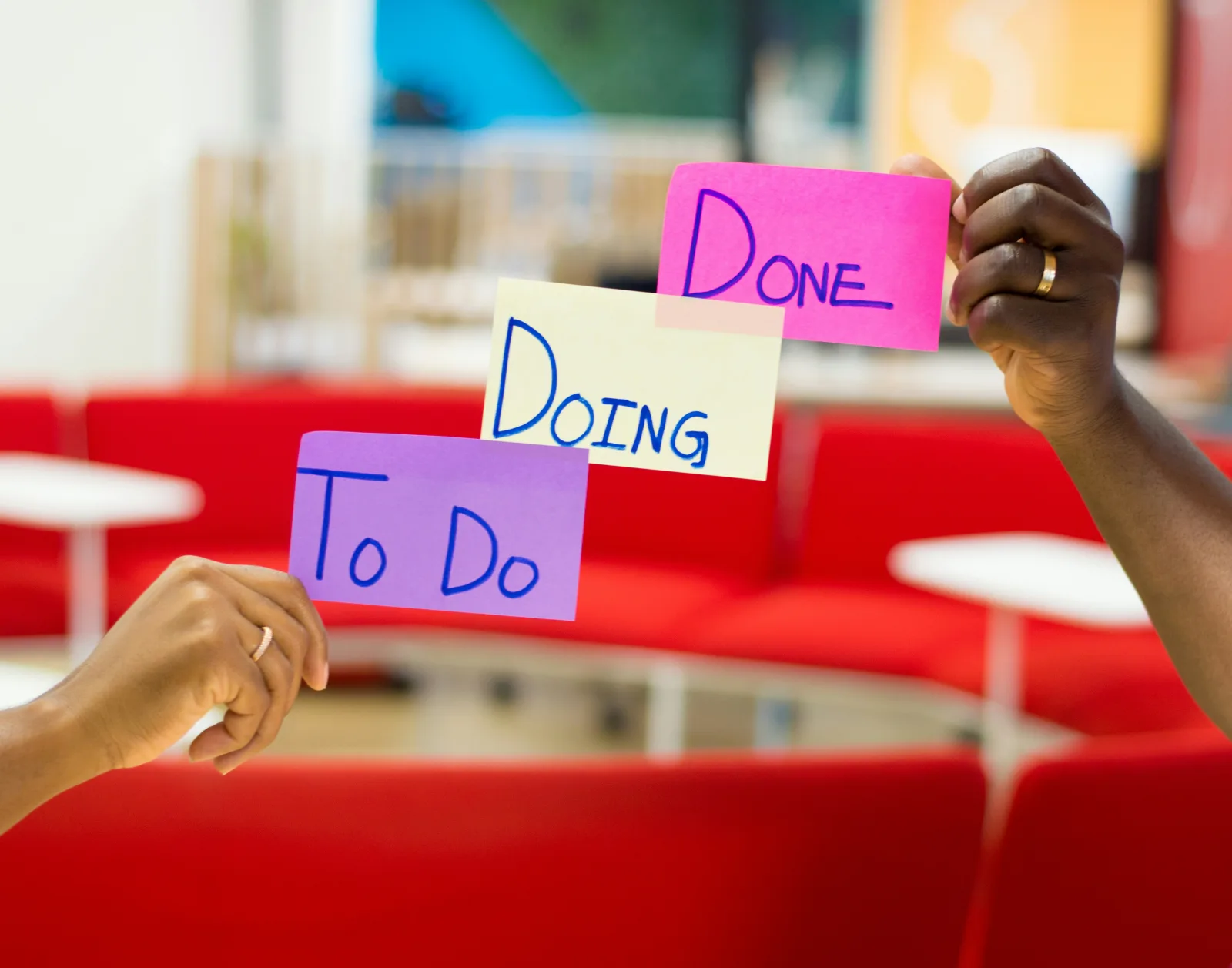 Two hands holding sticky notes labeled To Do, Doing and Done