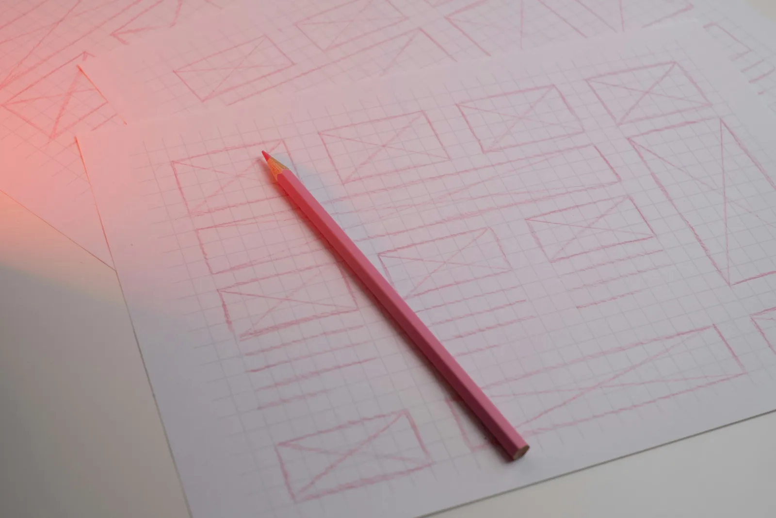Pink pencil resting on grid paper covered in hand drawn wireframe boxes