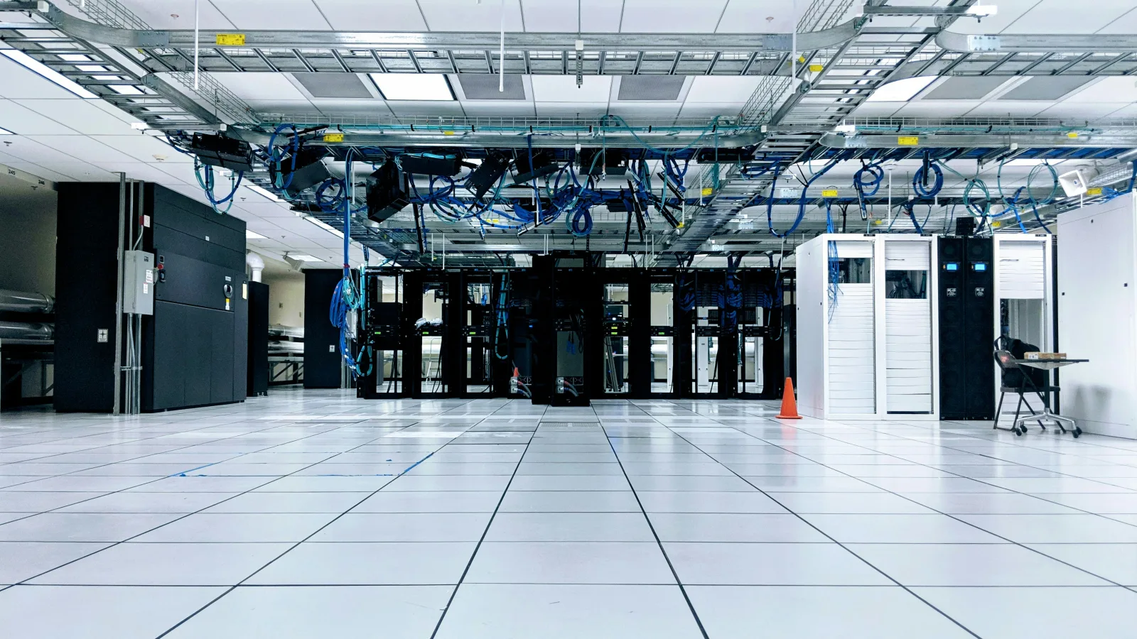 Rows of server racks under blue overhead cabling in a data centre hall