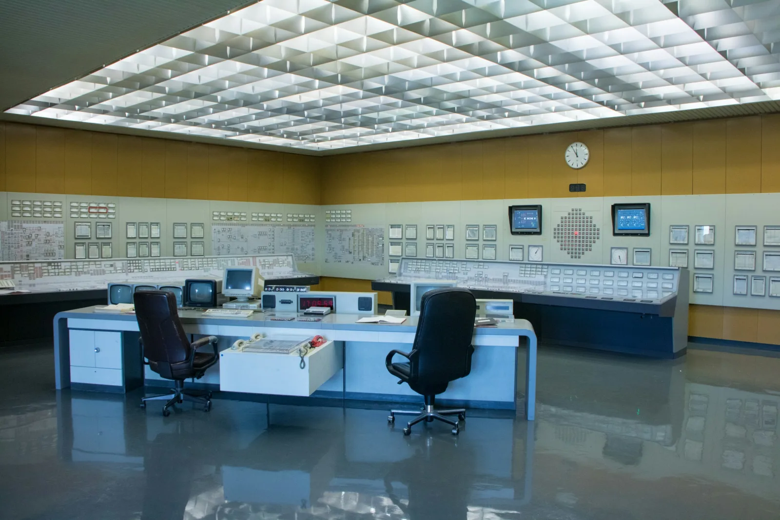 An empty operations control room with two chairs facing wall panels of gauges and screens