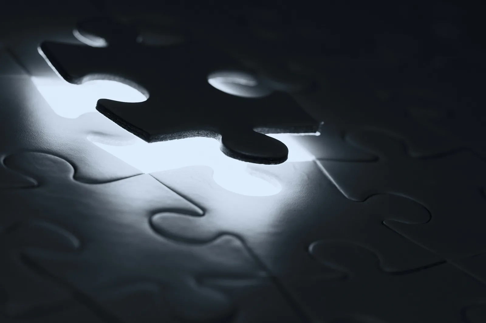 A dark jigsaw piece hovering just above the one empty slot in a puzzle, with light showing through the gap